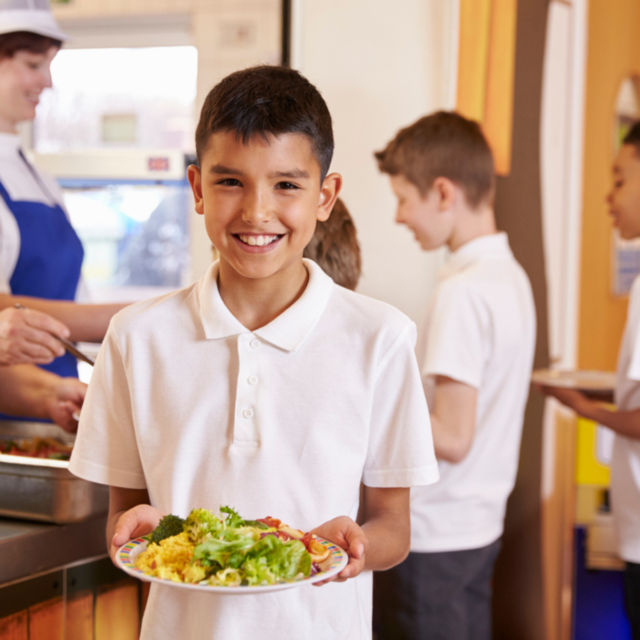 Child holding a school meal smiling, Free School Meals