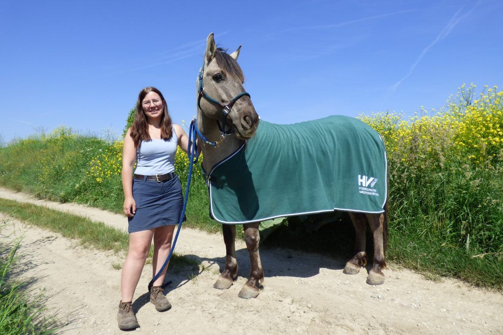 Symbolbild mit Pferdebesitzerin gemeinsam mit ihrem Pferd, das eine Pferdedecke trägt