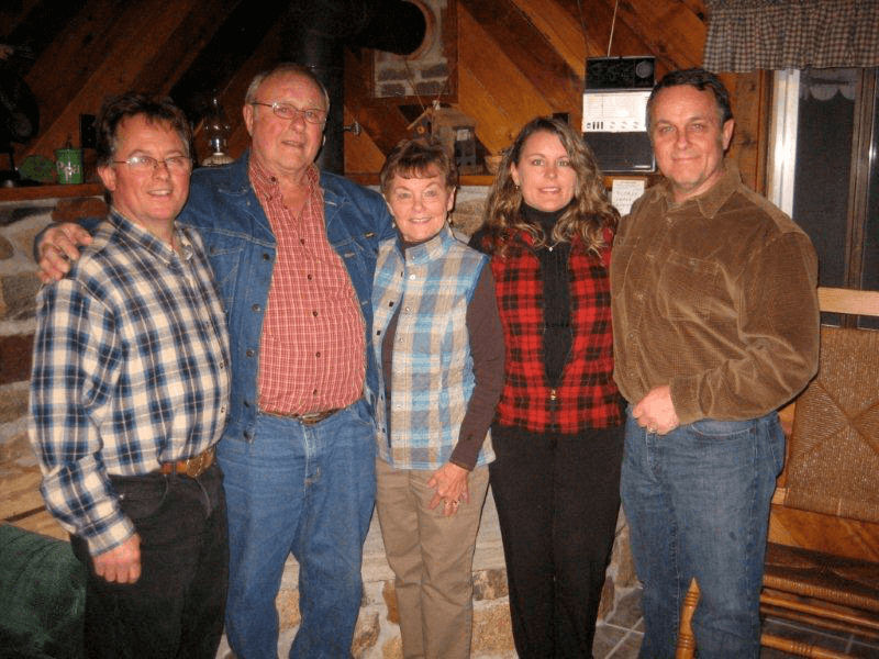 A family of five, hugging and facing the camera in a log cabin.