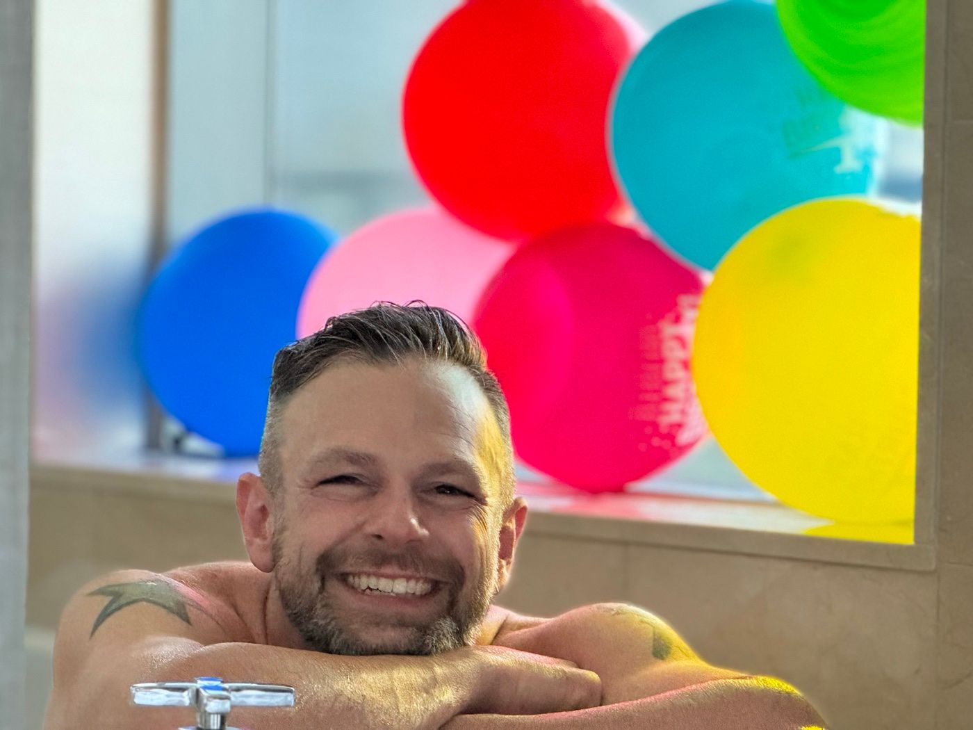 Joe smiling with a wall of colorful balloons behind him on his birthday