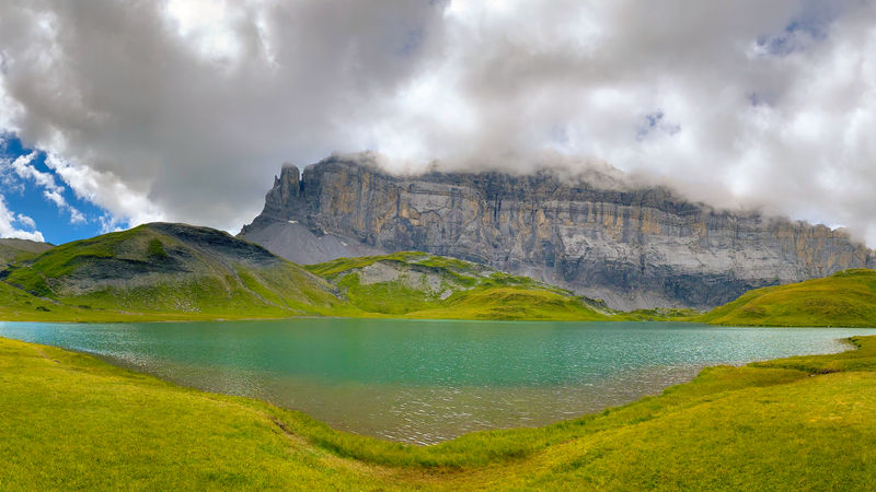 A westward view from the shore of Lake Anterne (Lac d'Anterne) toward the cloud-covered summit of Tête à l'Âne, rising to 2,804 meters, on the third day of the Tour des Fiz trek in the French Alps.