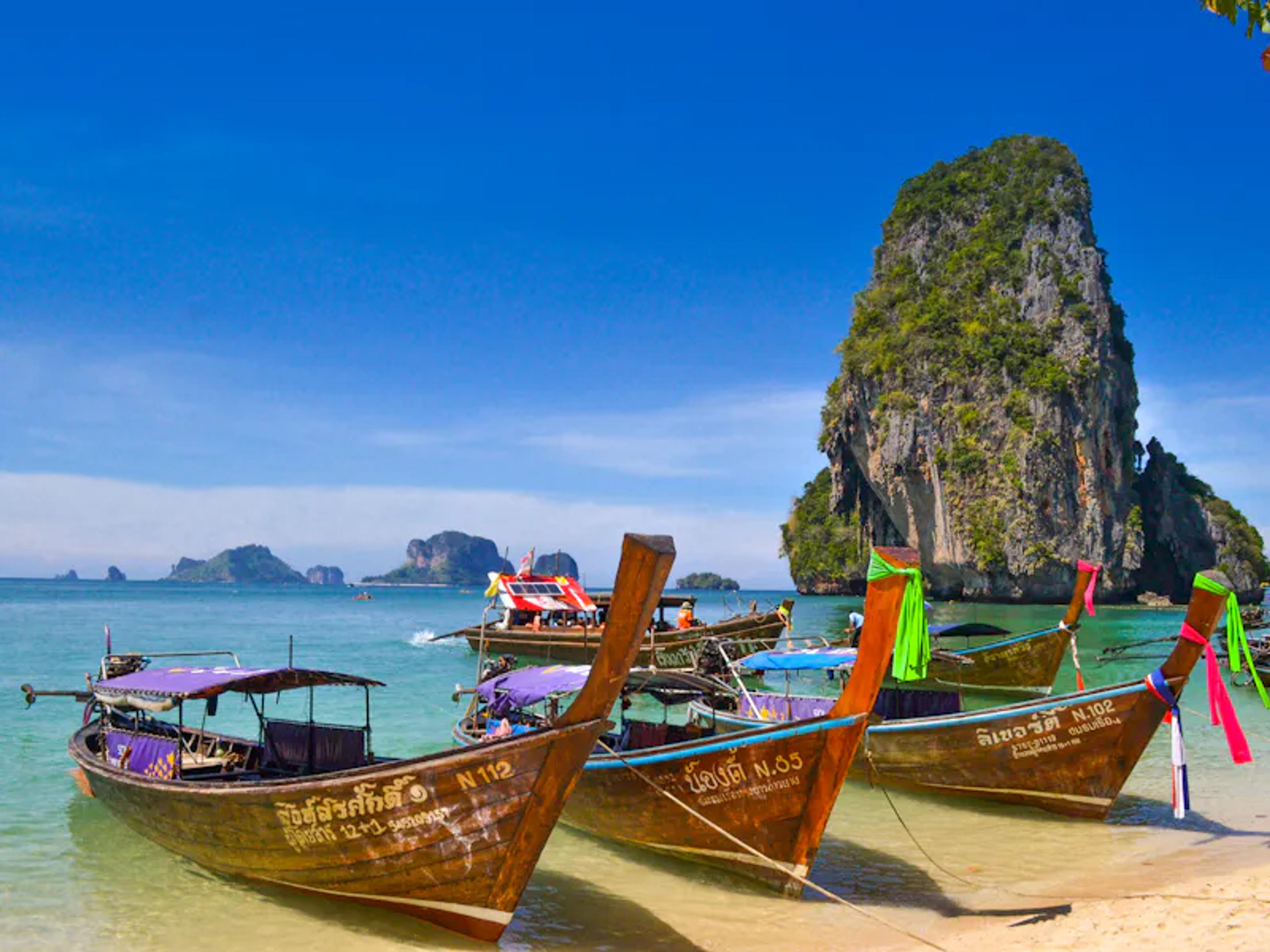 Longtail boats moored on a beach below towering limestone cliffs in Thailand