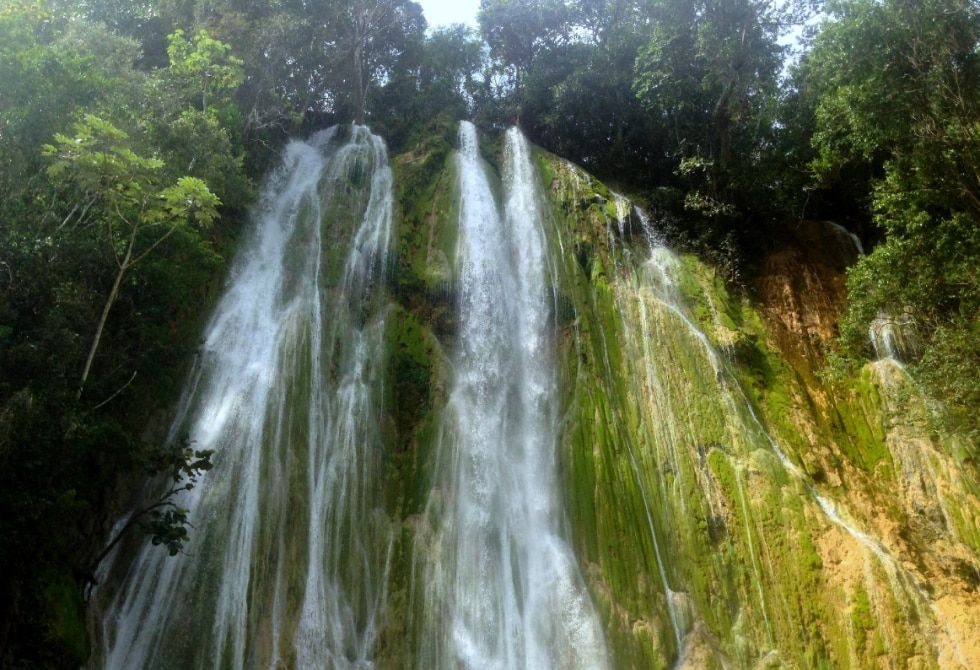 Las aguas cristalinas desembocan en una solidad pared rocosa y verde.