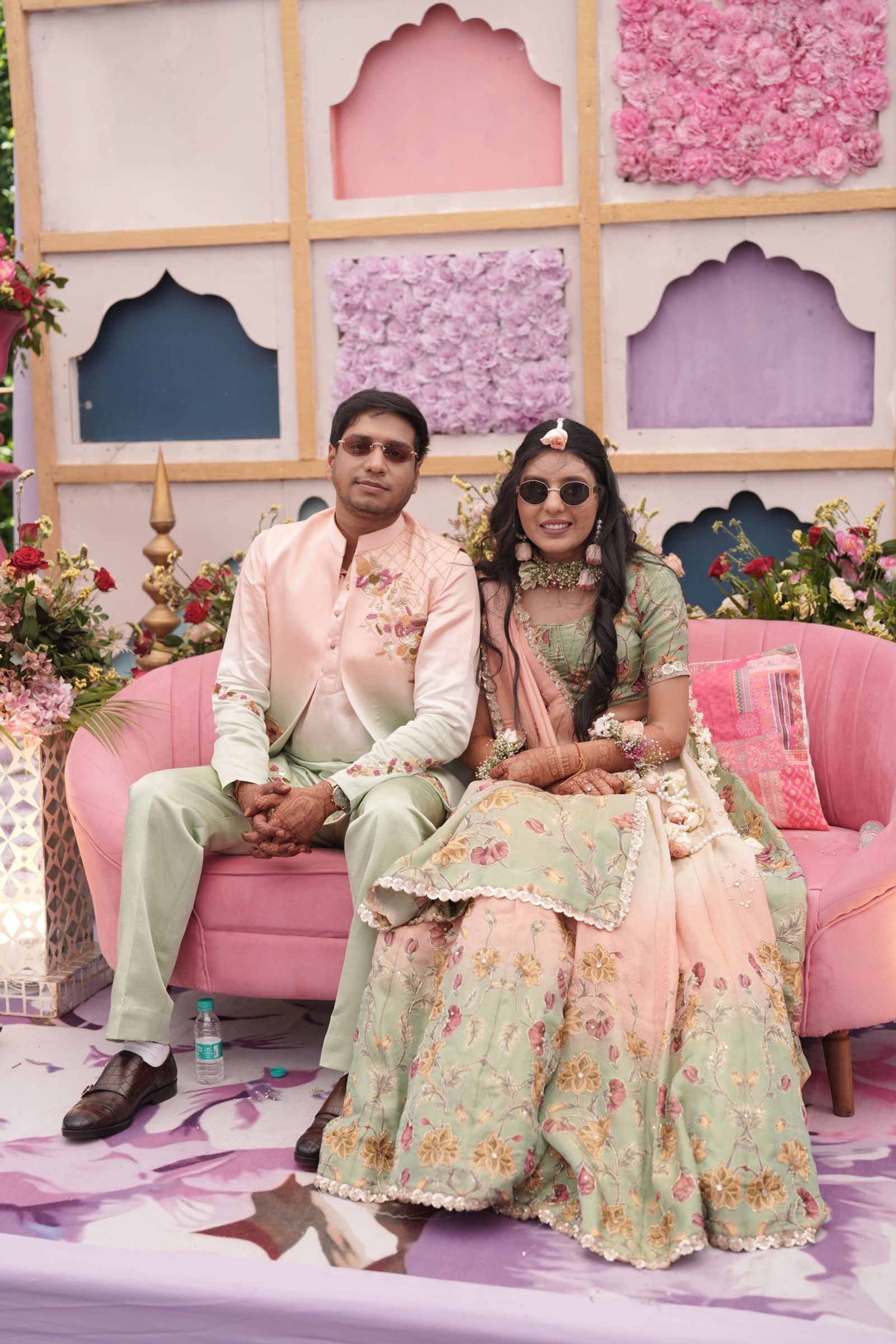 Ravi and Saloni on a pink sofa at the haldi, Saloni in sunglasses