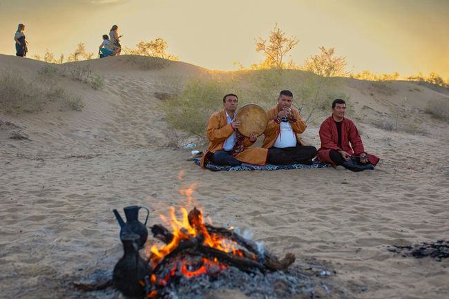 Musicians playing by a campfire amongst the sands at sunset