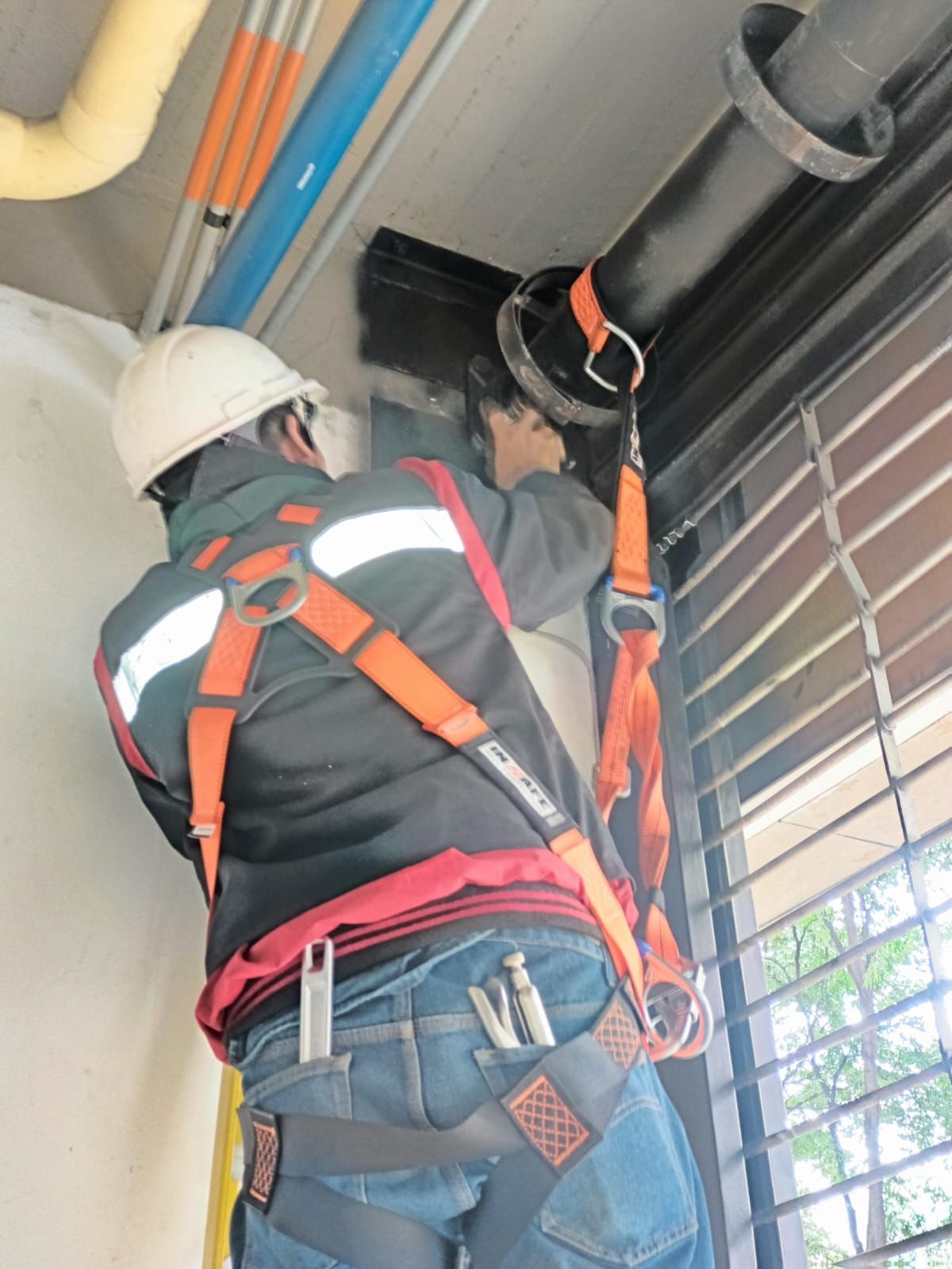 Técnico con casco y arnés trabajando junto al mecanismo superior de una puerta.