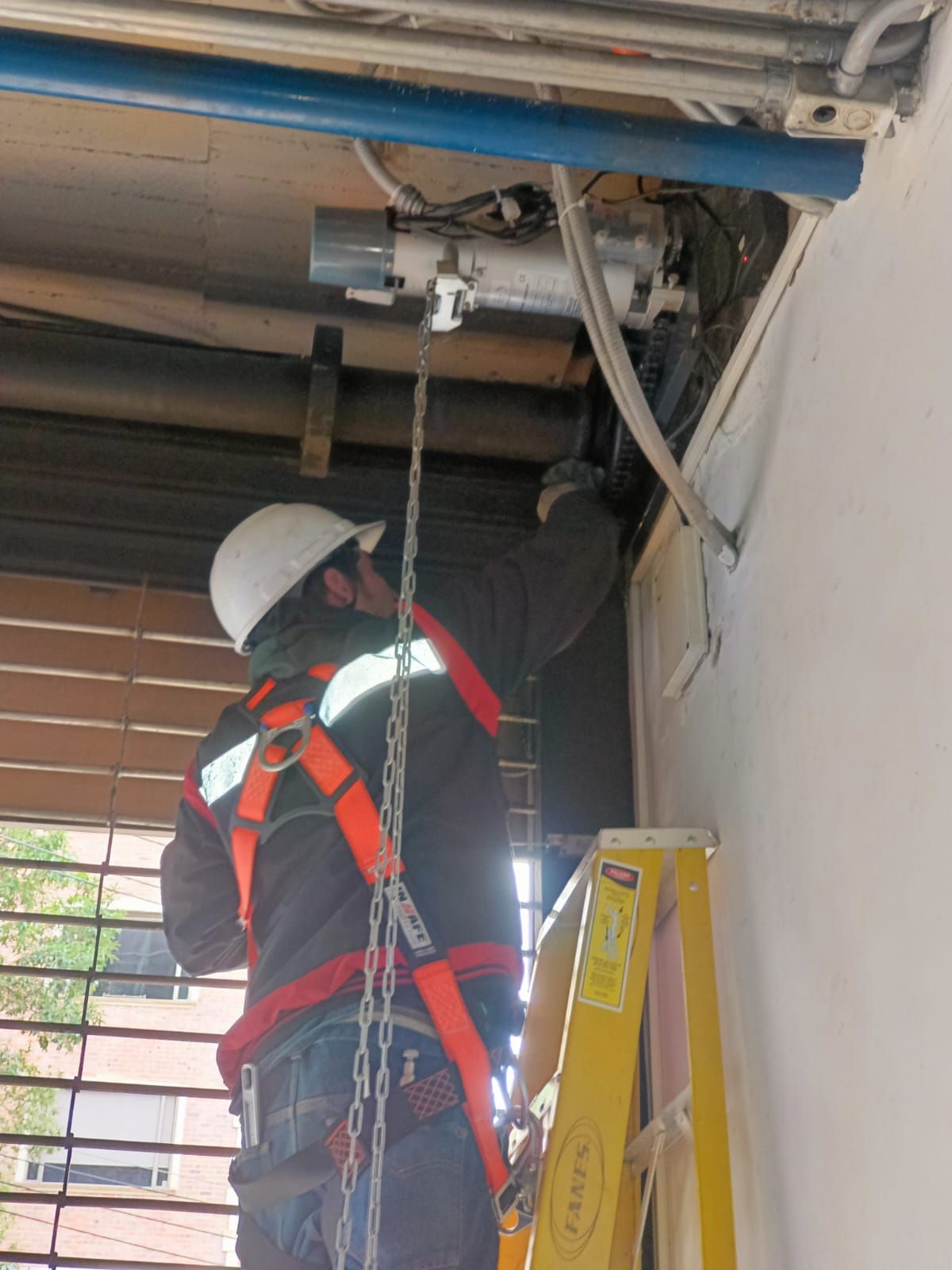 Técnico con casco y arnés interviniendo el mecanismo superior de una puerta automática.