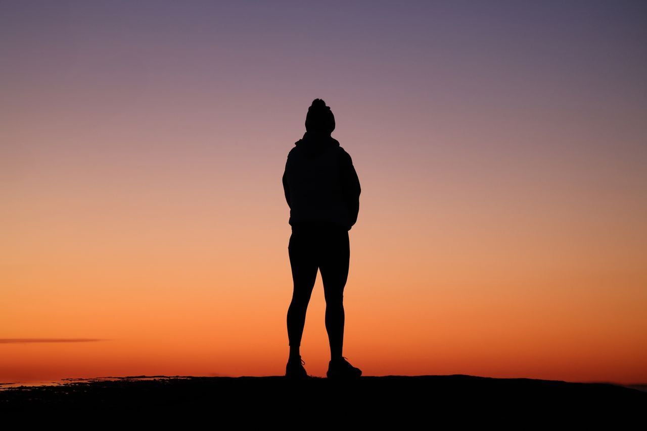 A lone figure standing against a wide sunset sky