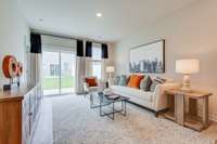 Cozy living room with sliding glass door opening out to patio. *Photos of model home - colors and finishes will vary in actual home under construction