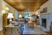 On the other side of the entryway is the large great room with original wood ceiling, gas fireplace and views out the front and back of the home. This view is facing toward the back.