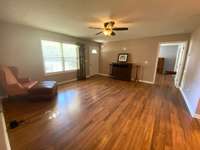 Walk into a large living room with laminate flooring, freshly painted walls, and ceiling fan