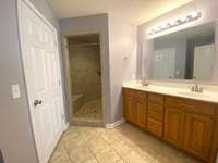Master Bathroom with double vanities, walk in tile shower with bench, tile floors and walk in closet