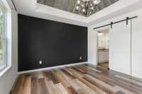 The primary bedroom boasts an accent wall, custom tray ceilings, and a barn door leading to the en suite bathroom