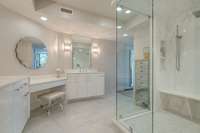 Sparkling white tile and superior finishes add elegance to this space. The frameless glass surround shower has tile all the way to the ceiling, a seated bench and rain shower head.