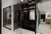 This custom design primary closet is enclosed with glass providing structure and a open feeling to the room.