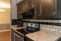 Galley kitchen with tile backslash and granite countertop that provides floor to ceiling of cabinets for storage. Right around the corner is the laundry area with washer and dryer to remain.