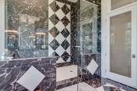 The marble tile and glass shower is a showpiece itself.