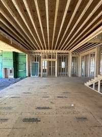 View of Great Room with fireplace, built-in cabinetry, slider doors that open onto covered outdoor living area and 13' ceiling with beams   *this home is under construction  Photo taken 1/11/24  *this home is under construction  Photo taken 1/11/24