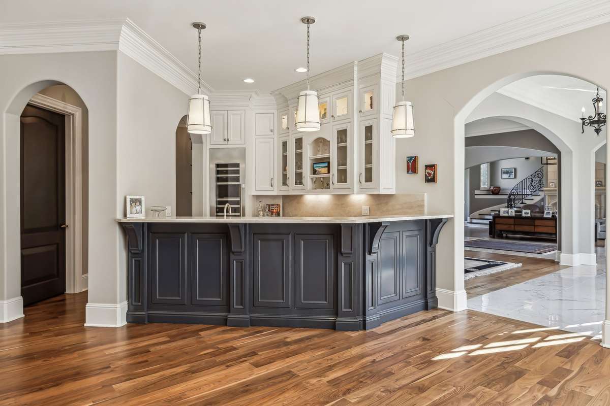 Just beyond, the wet bar continues the cohesive design with matching Taj Mahal countertops and backsplash, and ceiling-height cabinetry with illuminated glass-front uppers.