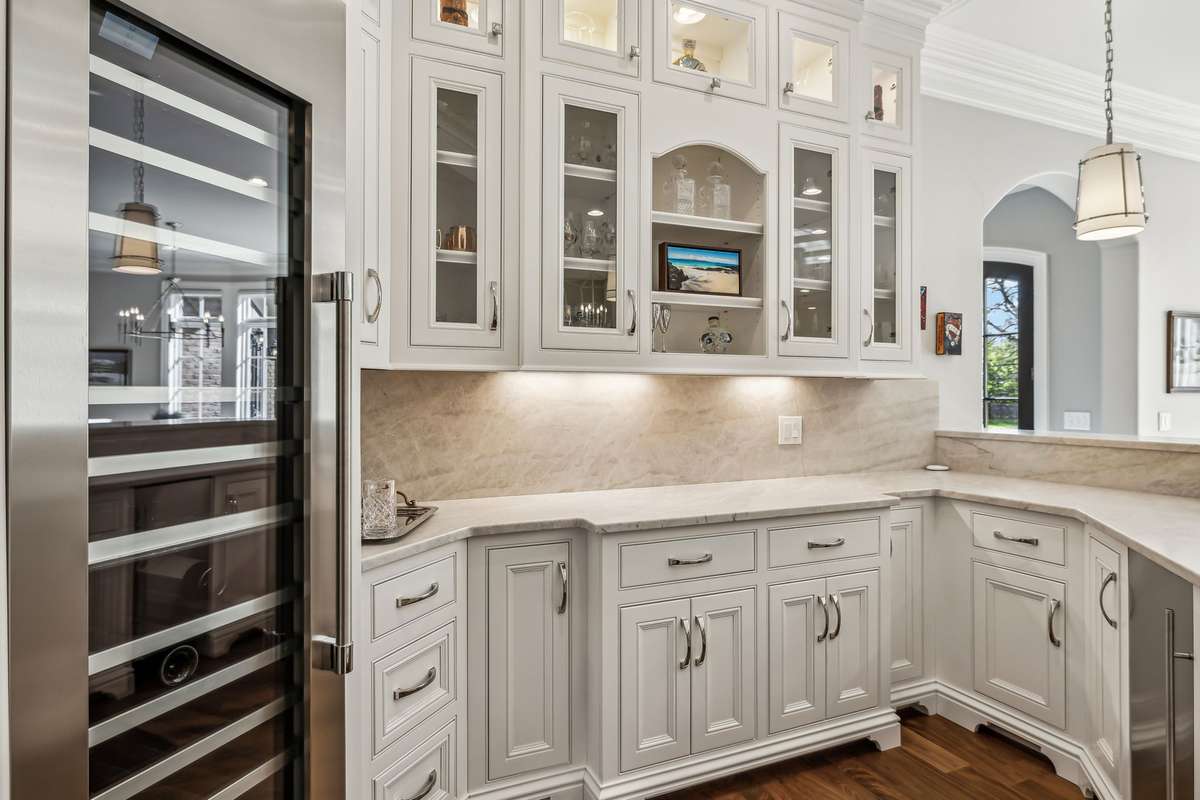 A Thermador 99-bottle wine fridge with three temperature zones, an additional sink, and polished nickel pendant lighting with linen shades make entertaining easy. Bar seating invites guests to gather, sip, and stay awhile.