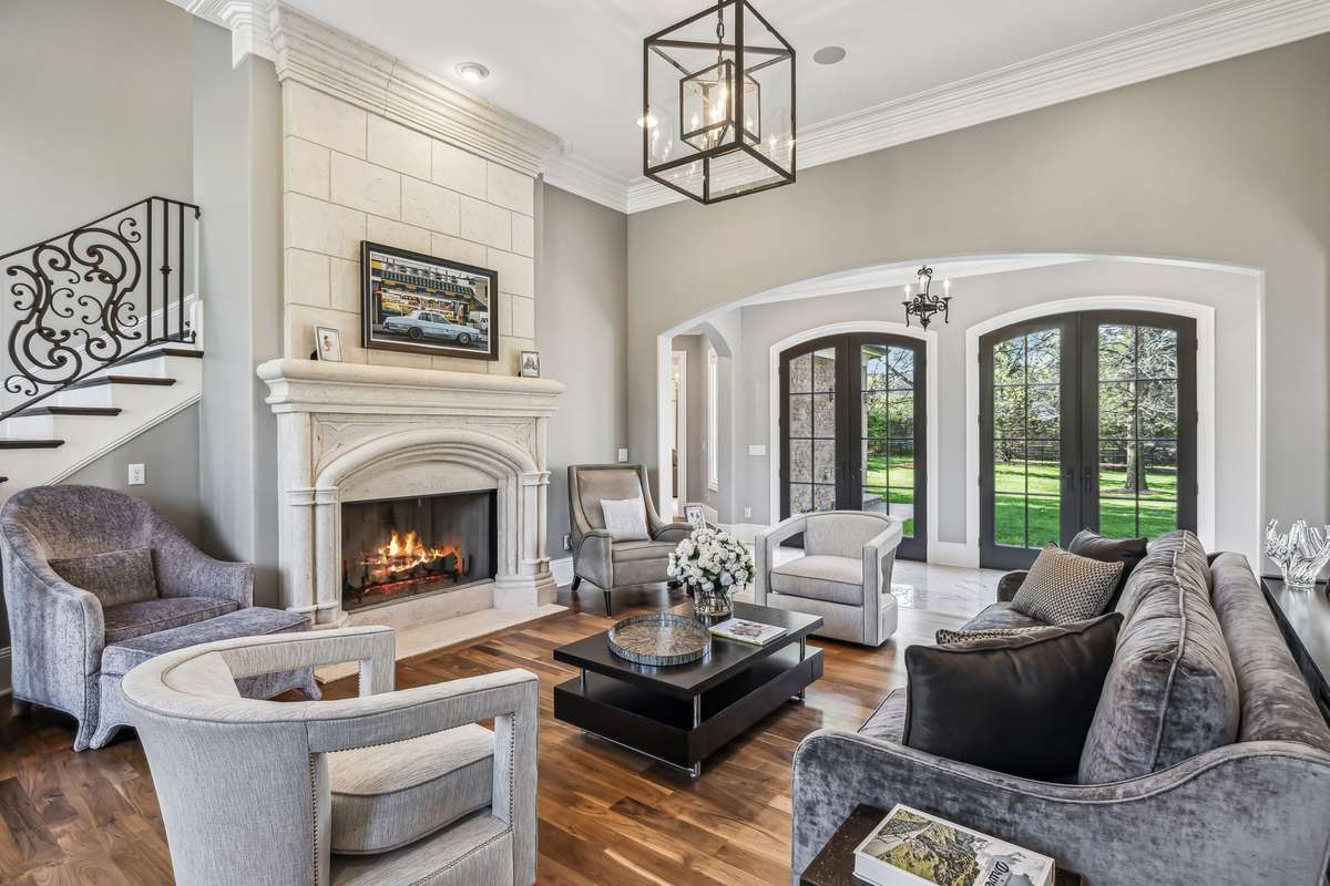 A lantern-style chandelier adds warmth and character from above, while the stately stone fireplace, complete with a hand-carved mantle and surround, becomes the room’s inviting focal point.