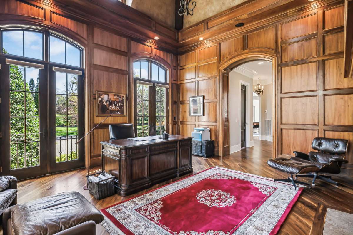 High-grade walnut flooring flows seamlessly into this richly appointed room, where full-wall wood trim and custom built-in bookcases frame a sleek gas fireplace w/a mounted TV above, perfect for getting work done or catching the game during a break.