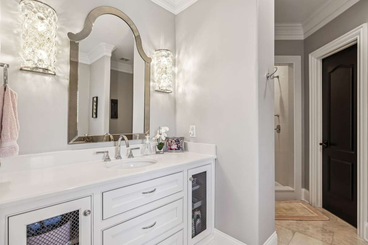 This beautifully appointed bath is a serene, spa-like retreat updated with high-end finishes such as premium Rohl fixtures at the sink, crystal sconces and a designer mirror that adds a touch of glamour.