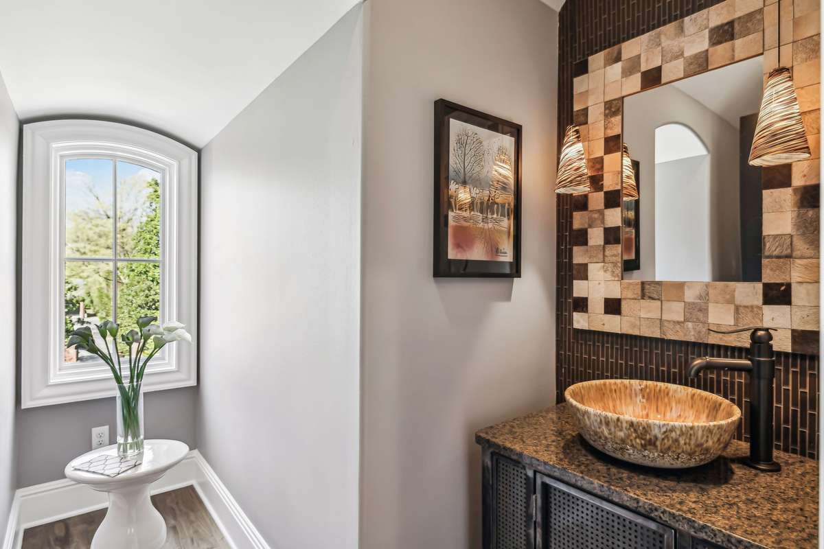 The Upstairs Powder Room features a furniture-style vanity w/a sleek granite countertop. A vessel sink adds a modern touch, while a tile-framed mirror & elegant pendant lights enhance the space’s sophistication.
