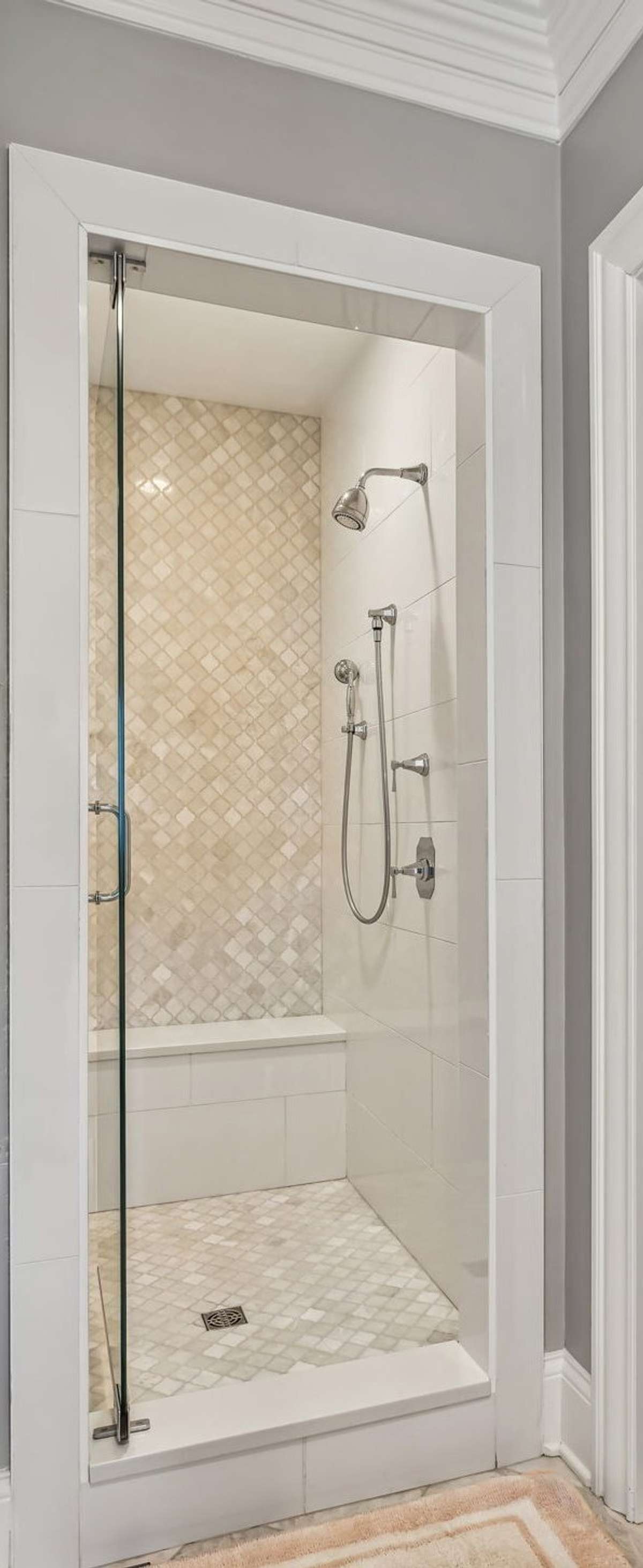 The walk-in shower is a true showpiece, featuring a marble arabesque accent wall and matching flooring, a built-in bench, and a sleek glass door.