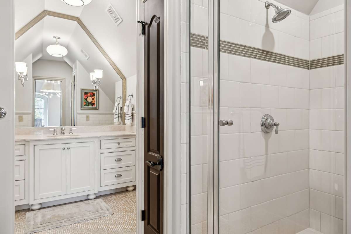 This beautiful bathroom features a vaulted ceiling and a walk-in shower finished with an elegant tile, creating a clean and modern aesthetic. A spacious vanity offers dual drawer stacks and ample cabinet storage to keep essentials organized.