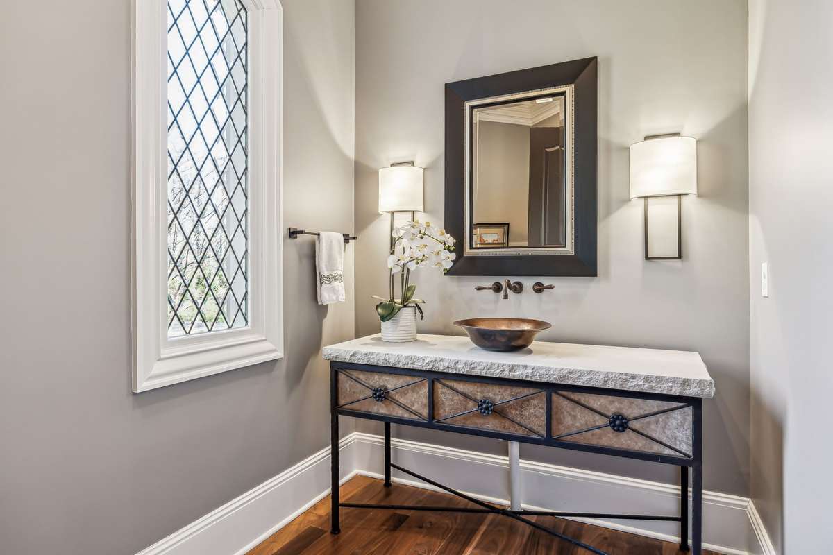 The main level 1/2 bath exudes sophistication w/a stone vanity & a copper sink paired w/floating faucets adds a touch of allure, while sconce lighting casts a warm glow. A framed mirror & a beveled diamond window & new toilet complete the space.