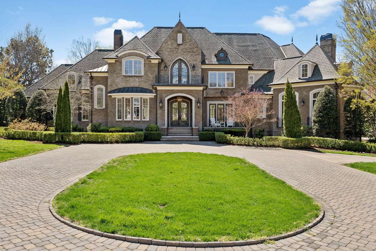 Breathtaking! The partially covered porch makes a striking impression, framed by a stone archway, gas lanterns, and intricate iron railings. Situated on 1.5-acre corner lot surrounded by lush, mature landscaping, this home offers a serene setting.