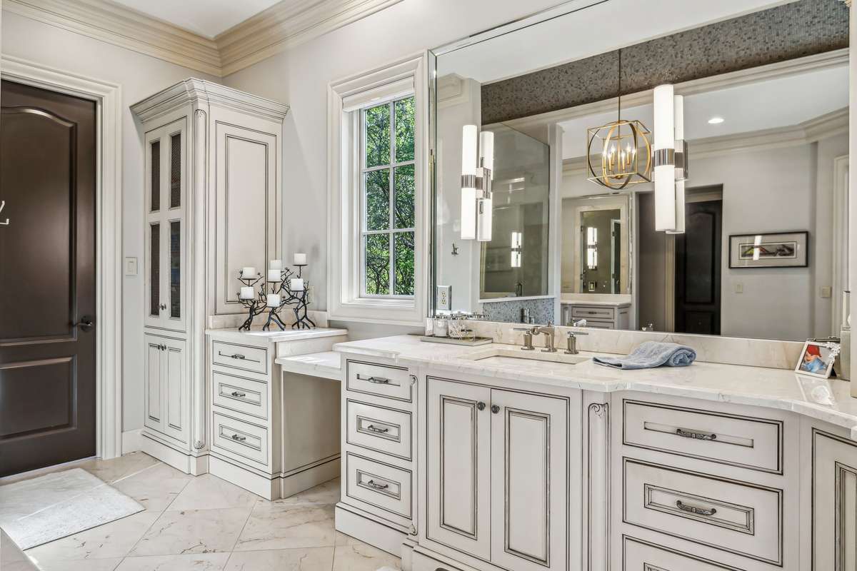 Separate vanities are thoughtfully designed, with spacious drawer stacks, knee space, oversized mirrors, soft sconce lighting, and luxurious marble countertops.