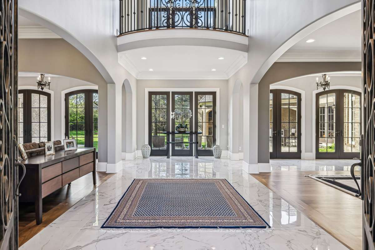 Your eyes are drawn to the stunning barrel-vaulted ceiling, where a glowing chandelier casts a soft light. Twin balcony's with intricate iron railings add a touch of romance, while a wall of windows and French doors flood the space with light.