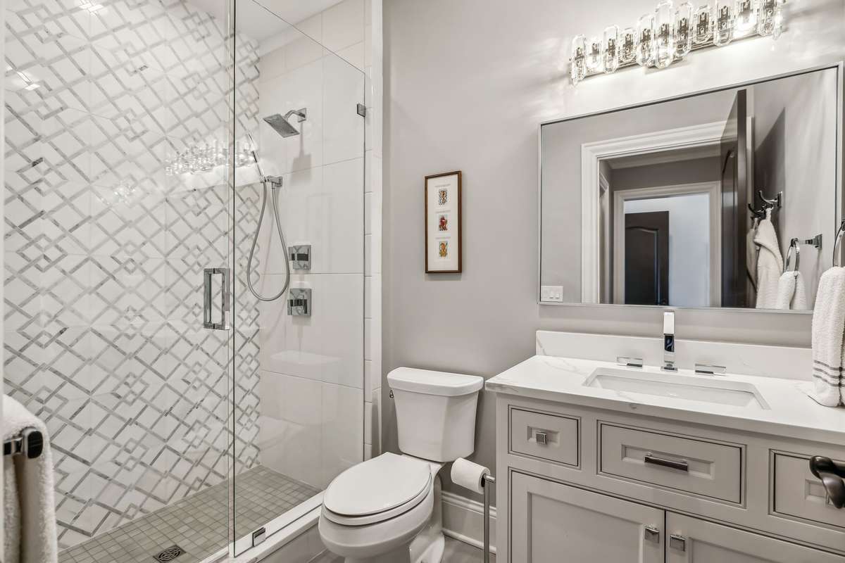 The Guest Bath features a sleek walk-in shower with a frameless glass enclosure, chrome fixtures, and a luxurious rain head paired with handheld sprayers. A striking Waterjet marble mosaic accent wall adds an elegant touch.