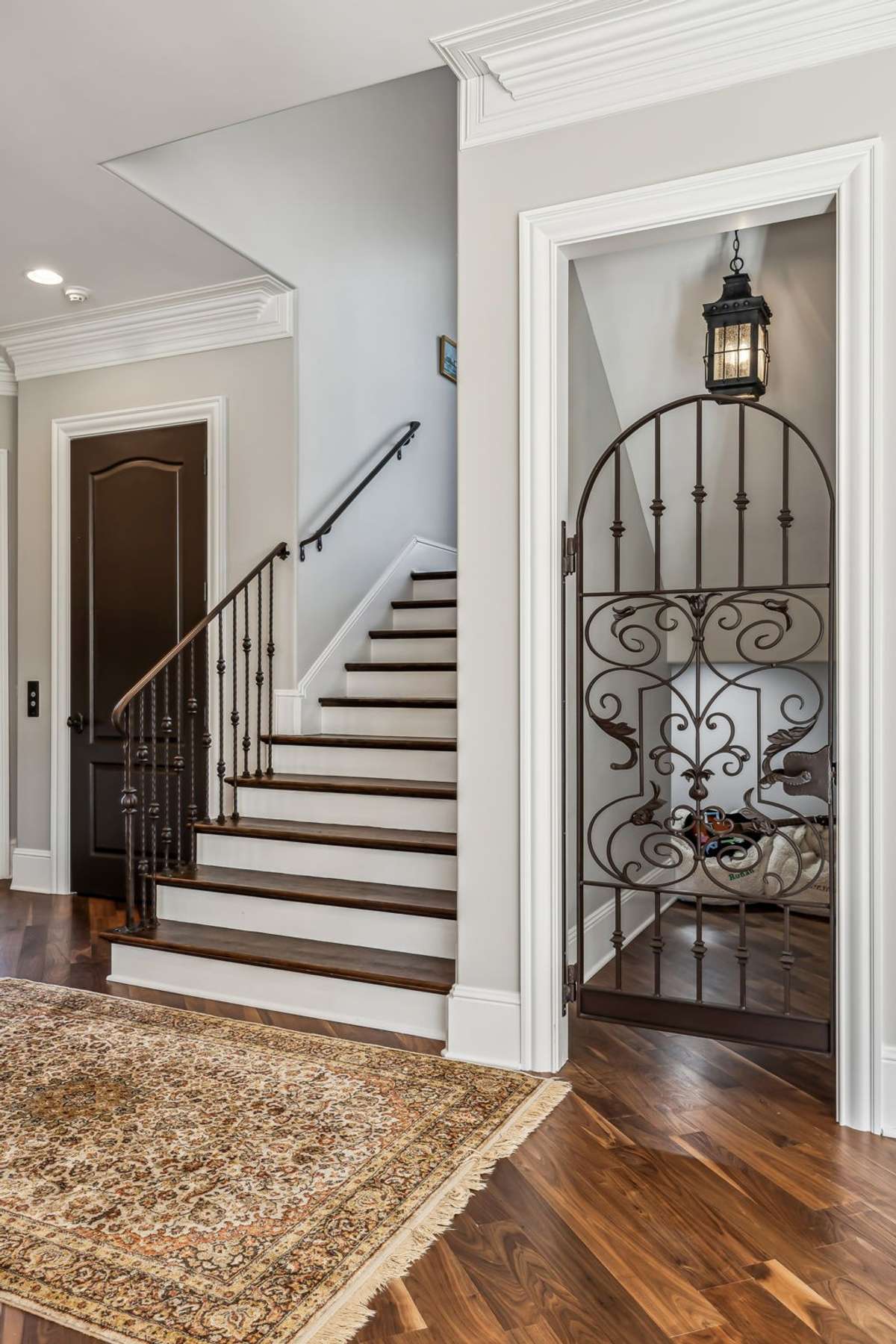 Beneath the curved staircase, a charming iron-gated nook—currently serving as a playful hideaway—offers exciting potential as a wine room or stylish extra storage.