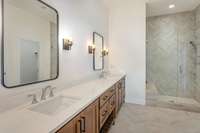 Primary bathroom features lovely tile shower, double vanities and sconce lighting