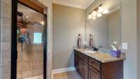 The walk-in shower in this bathroom is beautifully tiled, complemented by a sleek glass door that adds a touch of sophistication while ensuring a clear view of the space and one of the two granite countertop vanities in this his and hers bathroom!