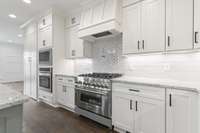 This gas range is surrounded by a custom backsplash and accompanied by a second wall oven and a microwave.