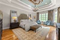 Primary bedroom suite with tray ceiling and big picture windows looking out to the wooded backyard.