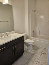 A full guest bathroom features quartz countertops and 12x24 floor tiles