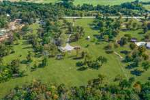 This aerial view is perfect to see what the front acreage looks like with driveway leading to property, home, parking, garage and barns.
