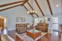 Walking through the front hall, past the main hallway, you enter this grand gathering room that features modern vibes and old-world warmth with the wagon wheel chandelier and real wood coffered ceilings.