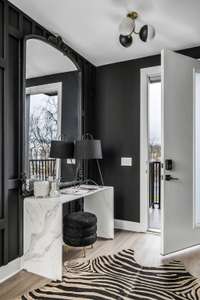 A rich and lustrous entryway welcomes your guests with a show-stopping custom paneled accent wall and dynamic statement lighting at the top of its high ceilings. A matte black and crisp white color palette throughout the home is bold and inviting.