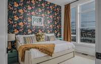 The next guest bedroom is bright and alluring, featuring expansive windows to welcome an abundance of natural light in the space. A delightful accent wall is adorned with depictions of Japanese koi, symbolizing success, ambition, and perseverance.