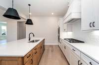 Gas cooktop, double ovens, wood hood, tiled backsplash, quartz counters, custom cabinets with soft close drawers and cupboards, custom lighting and upgraded plumbing fixtures