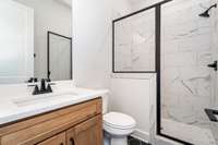 Guest bathroom down features tile shower, tile floor, quartz counter and custom cabinet