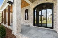 Blue stone front porch and curved, metal-frame double door entry with substantial gold hardware make for a dramatic entry