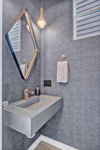 This main level powder room showcases a sleek modern design with gorgeous fixtures, a striking tiled ceiling and designer wallpaper.