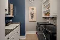 A conveniently situated laundry room off the kitchen area is equipped with custom cabinetry & sink for easy clean up